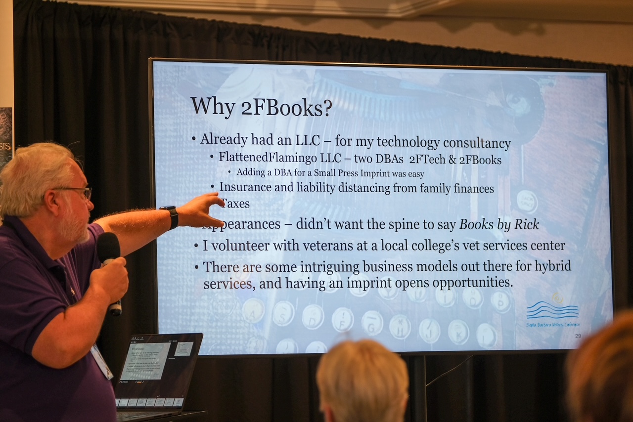 Speaker in a purple polo with a microphone points to a slide titled 'Why 2FBooks?' at a conference.